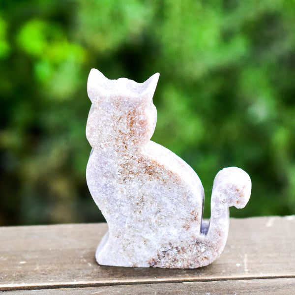 Whyte Quartz Grade A Pink Amethyst Sitting Cat with Rust and Pink colors on wood table with greenery outdoors