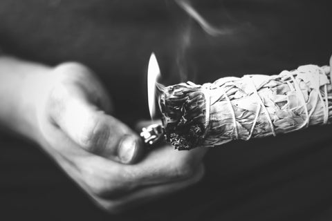 image of a persons hand lighting a sage stick with a lighter and the sage is burning