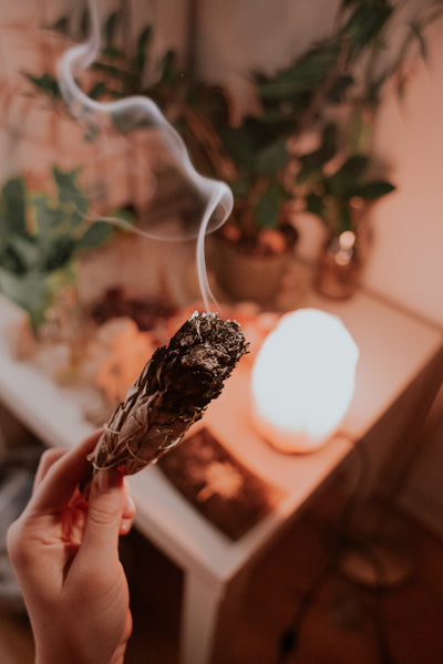 Image of a hand holding a burning sage stock with a table and light in the background